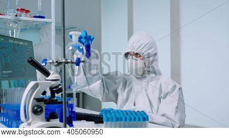 Medical Scientist With Coverall In Laboratory Room Performs Tests With Blue Liquid On Test Tube Typi