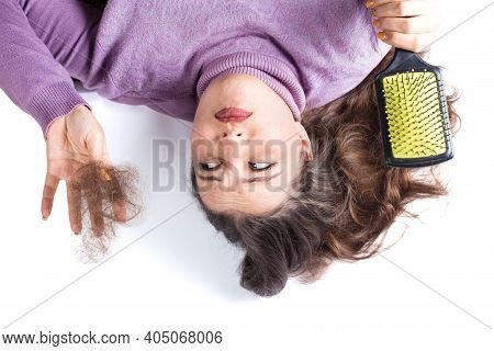 Young Woman Hlding Bunch Of Loss Hair And Hair Brush On A White Background.