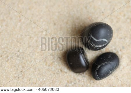 Three black stones in the sand.