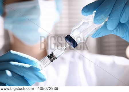 Woman Filling Syringe With Vaccine From Vial On Blurred Background, Closeup