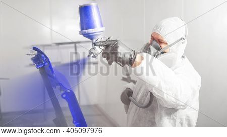 Car Painter Spraying Blue Paint With Spray Gun On Vehicle Element In Paint Chamber.