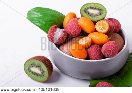 Lychee, Kiwi And Kumquat In A Gray Ceramic Bowl On The White Table. Assorted Tropical Fruits