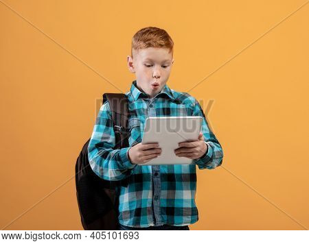 Amazed Ginger Boy Schooler With Backpack Using Digital Tablet, Looking At Pad Screen With Shocked Ga