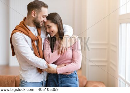 Loving Arab Husband Embracing Young Wife Standing At Home. Couple Enjoying Time Together. Happy Marr