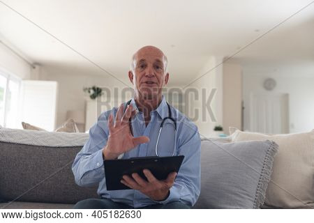Senior caucasian male doctor having a video call using a digital tablet at home. medical professional worker.