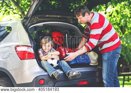 Little Kid Boy Sitting In Car Trunk Just Before Leaving For Summer Vacation. Dad Packing Suitcases. 