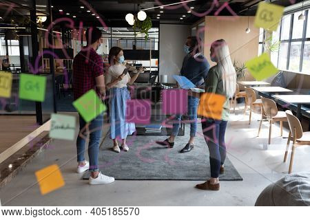 Diverse group of business people working in creative office. group of people wearing face masks and discussing work. social distancing protection hygiene in workplace during covid 19 pandemic.