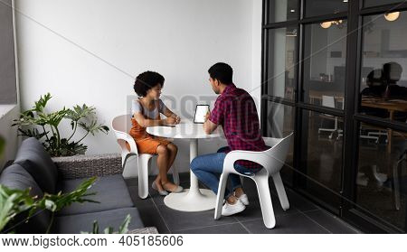 Two mixed race business people working in creative office. two people sitting and discussing work. business people and work colleagues at a busy creative office.