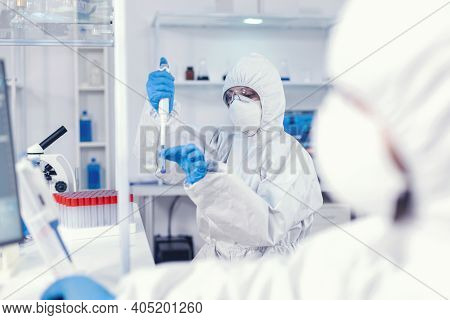 Medical Scientist Developing Coronavirus Vaccine In Science Lab Holding Micropipette. Team Of Microb