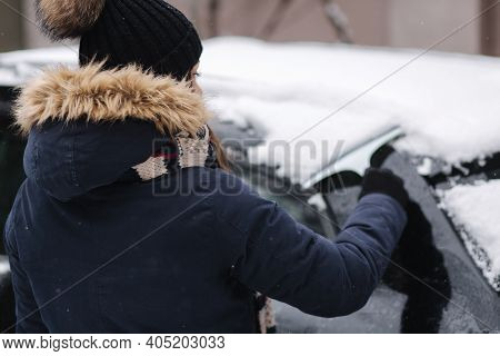 A Woman Is Cleaning Snowy Window On A Car With Snow Scraper. Pretty Woman Warmy Dressed Clean Her Ca