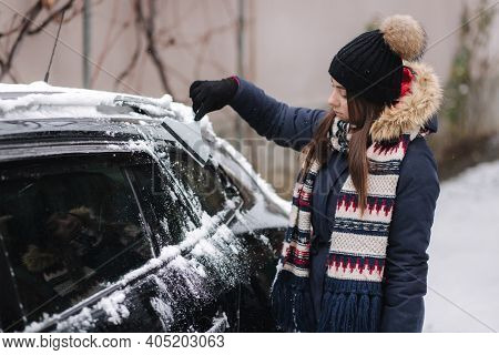 A Woman Is Cleaning Snowy Window On A Car With Snow Scraper. Pretty Woman Warmy Dressed Clean Her Ca