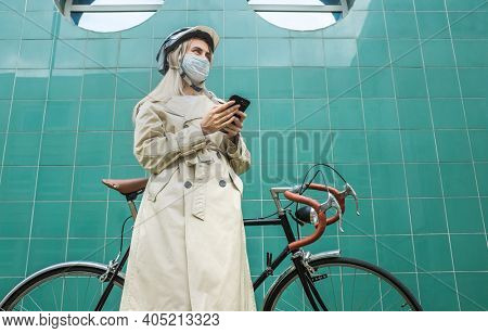 Woman in protective maskin, in helmet using her smartphone device. Female go to work on his sport retro bike. Girl standing on green background.