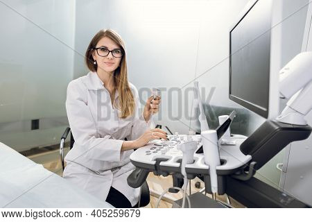 Smiling Pleasant Pretty Woman Doctor With Ultrasound Transducer In Hand, Working On Modern Ultrasoun
