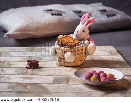 Easter Basket With A Rabbit Figurine With Multicolored Chocolate Eggs On A Light Tray Standing On A 