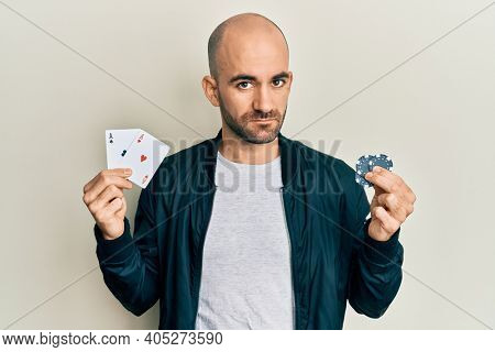 Young hispanic man playing poker holding casino cards and chips relaxed with serious expression on face. simple and natural looking at the camera. 