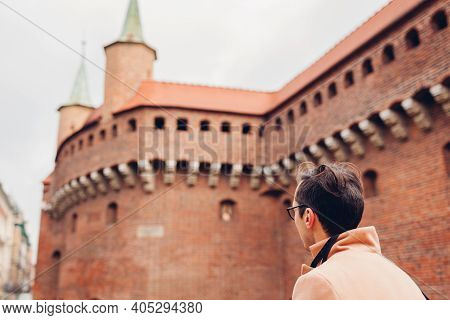 Tourist Looking At Barbikan Gate In Krakow City, Poland. Barbakan Museum. Man Traveler Enjoys Sights
