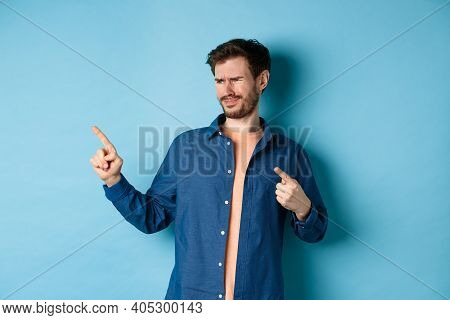Skeptical Young Man Pointing And Looking Left With Disappointment, Cringe From Something Bad, Standi