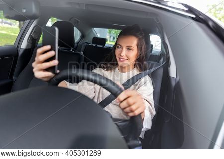 safety and people concept - happy smiling young woman or female driver driving car and taking selfie with smartphone