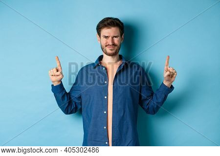 Skeptical Young Man Frowning And Squinting, Cringe From Something Disgusting, Standing On Blue Backg