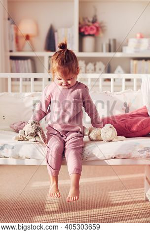Toddler Baby Girl Sitting On The Bed In Sunlit Nursery Room At Home
