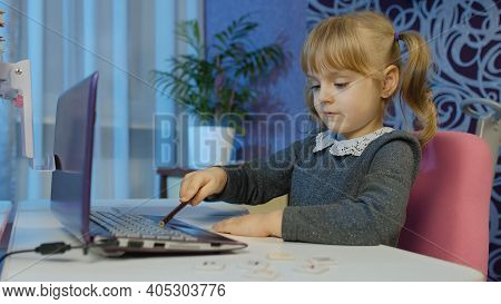 Child Schoolgirl Learning Lessons Being At Home Sitting At Table Using Laptop Digital Computer. Port