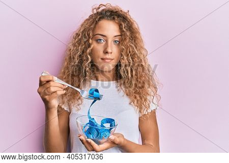 Beautiful caucasian teenager girl eating measure meter doing diet for weight loss relaxed with serious expression on face. simple and natural looking at the camera. 