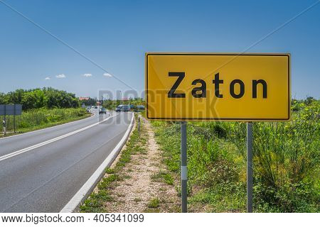 Large Yellow, Zaton City Welcome Sign With Cars On A Road And Green Field On Roadside, Croatia
