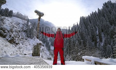 The Guy Stands On The Edge Of The Hill And Enjoys The View. Looks At A Snowy Gorge With High Mountai