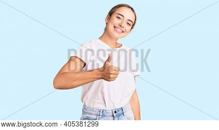 Young beautiful blonde woman wearing casual white tshirt doing happy thumbs up gesture with hand. approving expression looking at the camera showing success. 