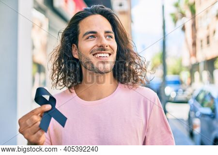 Young hispanic man smiling happy holding mouring black ribbon at city.
