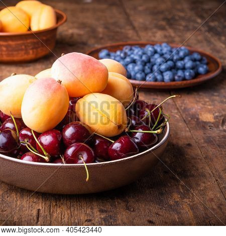 Bowl With Berries Cherries And Apricots On An Old Wooden Rustic Table Close-up Against A Background 