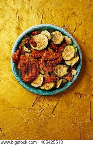 high angle view of a rustic green plate with some slices of dried tomato and zucchini, served as appetizer or snack, on a golden textured surface