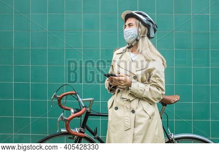 Woman in protective maskin, in helmet using her smartphone device. Female go to work on his sport retro bike. Girl standing on green background.