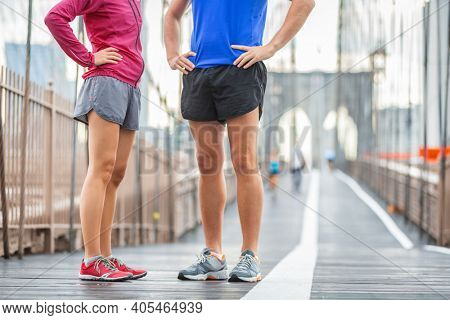 Runners legs training on Brooklyn bridge talking together before morning training run wearing run shorts and running shoes. Sports clothing concept, couple woman and man.