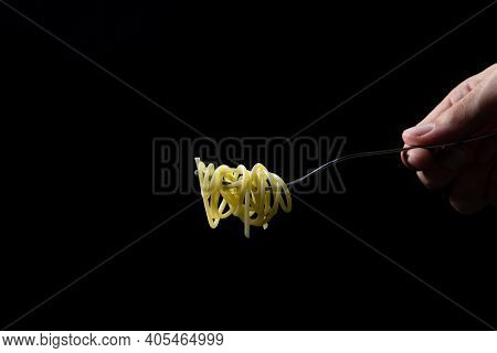 Spaghetti On A Black Background. Boiled Spaghetti On A Fork. Isolated Spaghetti. Male Hand Holding A