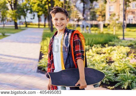 Guy Of 9 Years Old Riding Skateboard On Sunny Road In The Evening In The City Park. Holding Flutteri