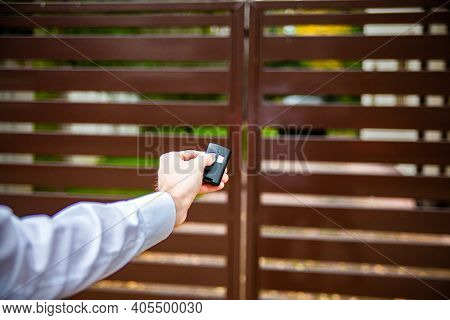 A Male Hand Pushing A Button On A Remote Control To Open An Entrance Gate.