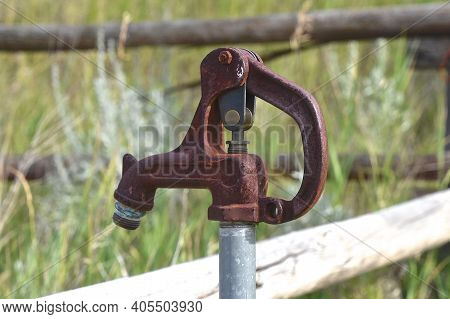 An Old Water Spigot Is Located Among Rails Of A  Corral Fence.