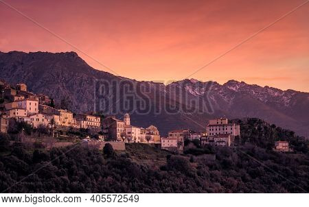 Orange Sunset Over The Ancient Village Of Belgodere In The Balagne Region Of Corsica With Snow Cappe