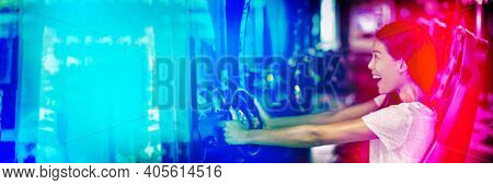 Asian woman playing car racing game at japanese gaming cyber arcade cafe. Driving game machine girl having fun playing racing car videogame driving virtual sports cars simulator banner.