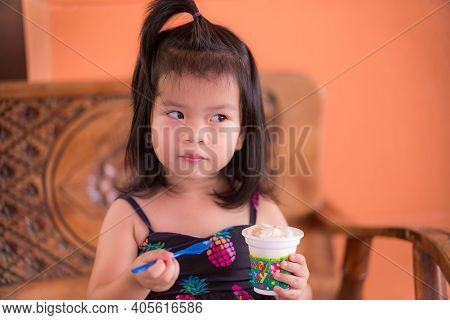 Cute Child Glanced At The Side. Make A Curious Face. Two Hands Holding Spoon Plastic And Ice Cream C