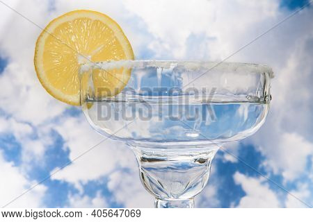 Coupe Cocktail Glass With A Lemon Wagon Wheel Garnish And Sugar Rim Against Cloudy Sky.
