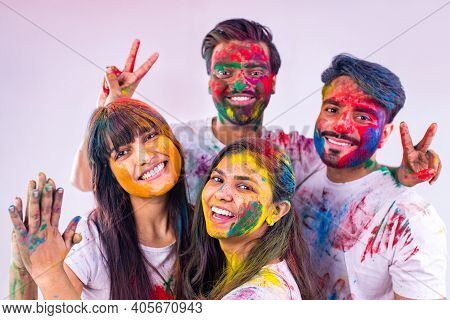 Four Indian Students Painted In Colors Celebrating Holi Festival In Studio White Isolate Background