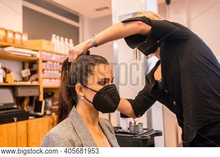 Hairdresser With Face Mask Combing The Client\'s Hair. Reopening With Security Measures Of Hairdress