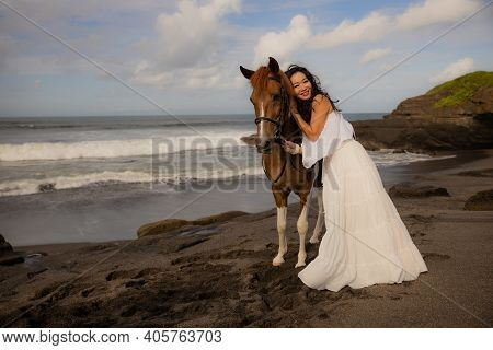Smiling Woman Leading Horse By Its Reins. Cuddling Horse. Love To Animals. Asian Woman Wearing Long 