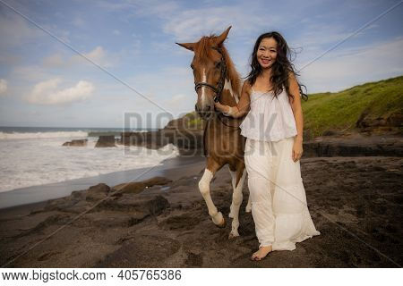 Smiling Woman Leading Horse By Its Reins. Horse Riding On The Beach. Human And Animals Relationship.