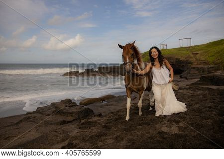 Happy Woman Leading Horse By Its Reins. Horse Riding On The Beach. Human And Animals Relationship. A