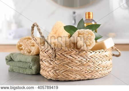 Natural Loofah Sponges In Wicker Basket And Towel On Table Indoors