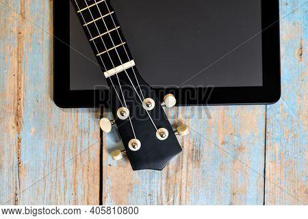 Tablet And Ukulele On Wooden Table With Space For Text. Online Learning To Play Hawaiian Guitar. Uku