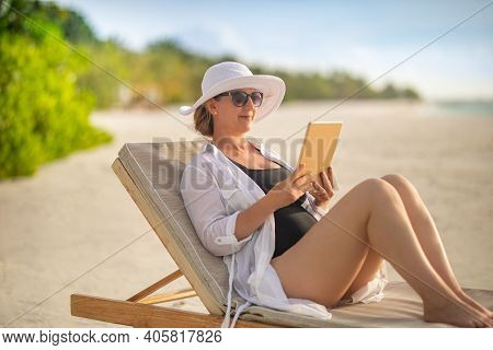 Woman Holding Tablet Computer Sitting On The Beach In Deck Chair And Enjoying Sunset Sunlight, Sea H